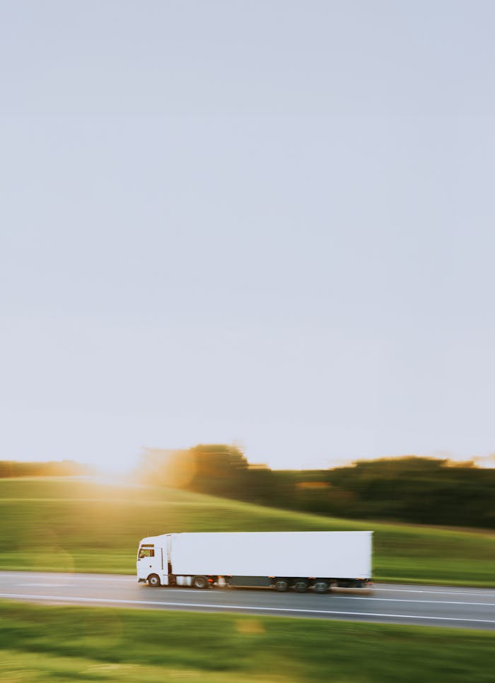 White cargo truck speeding through Vitebsk countryside at sunrise, symbolizing transportation and logistics.